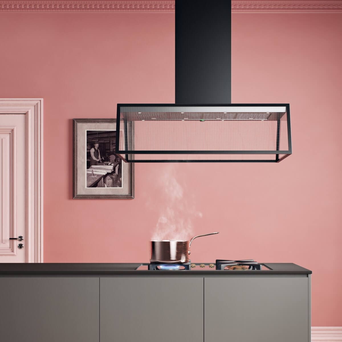 Frihängande köksfläkten Prisma i svart utförande ovanför köksö i minimalistisk kök med rosa toner.