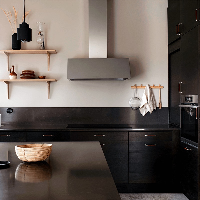 Vägghängda köksfläkten Aero i rostfritt utförande sticker ut i bland det minimalistiska kökets mörkare detaljer.